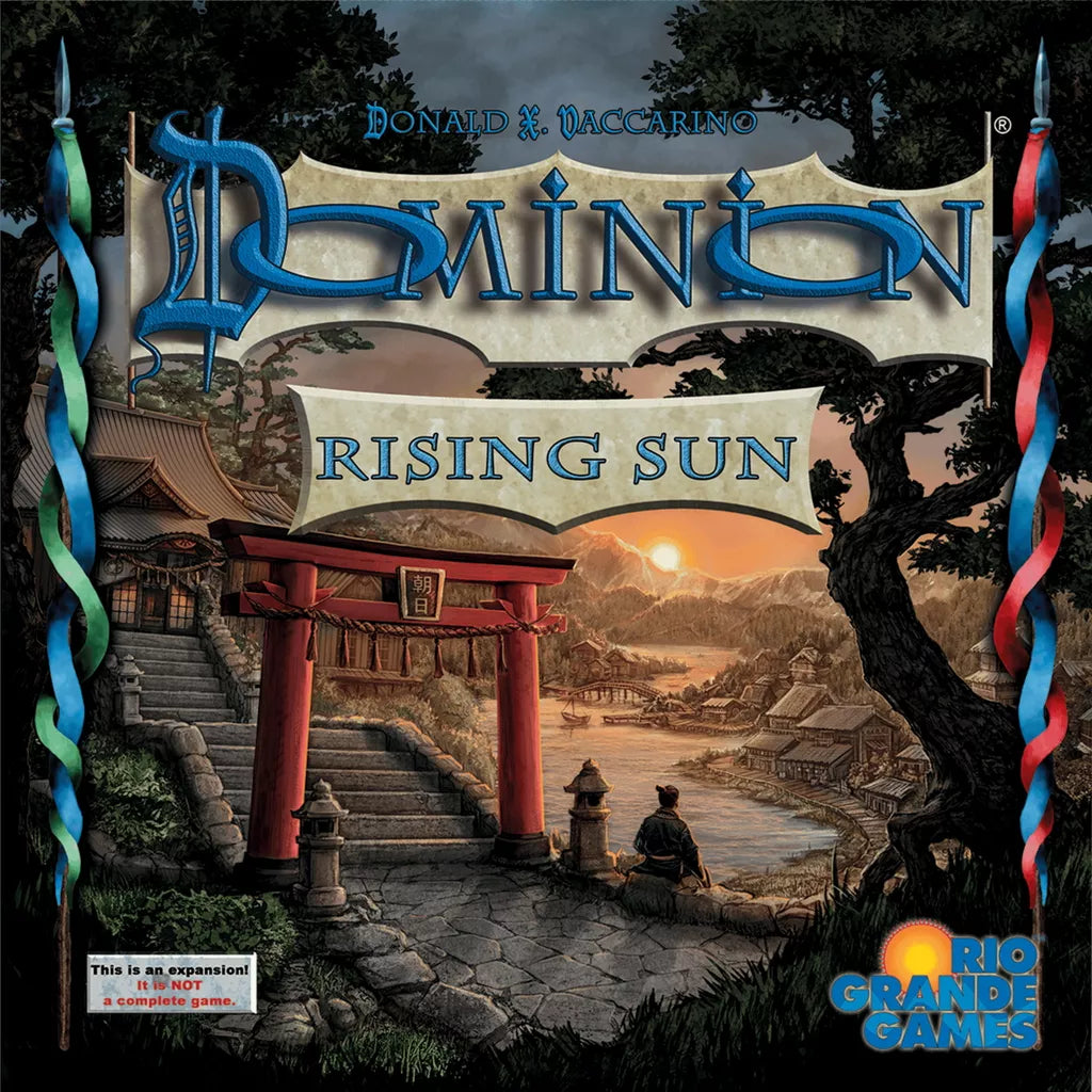 The cover of Dominion: Rising Sun Expansion by Rio Grande Games features a riverside Japanese village at sunset, a torii gate, mountains, new game cards hints, and the title in large stylized letters for this vibrant expansion.