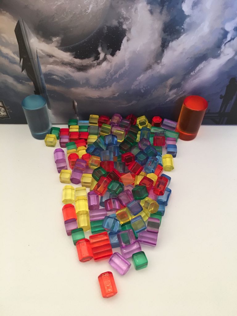 A scatter of small, colorful plastic tokens and orange and blue cylinders from Red Raven Games' Empires of the Void II pops against a sci-fi backdrop—ideal for fans of epic space strategy games.