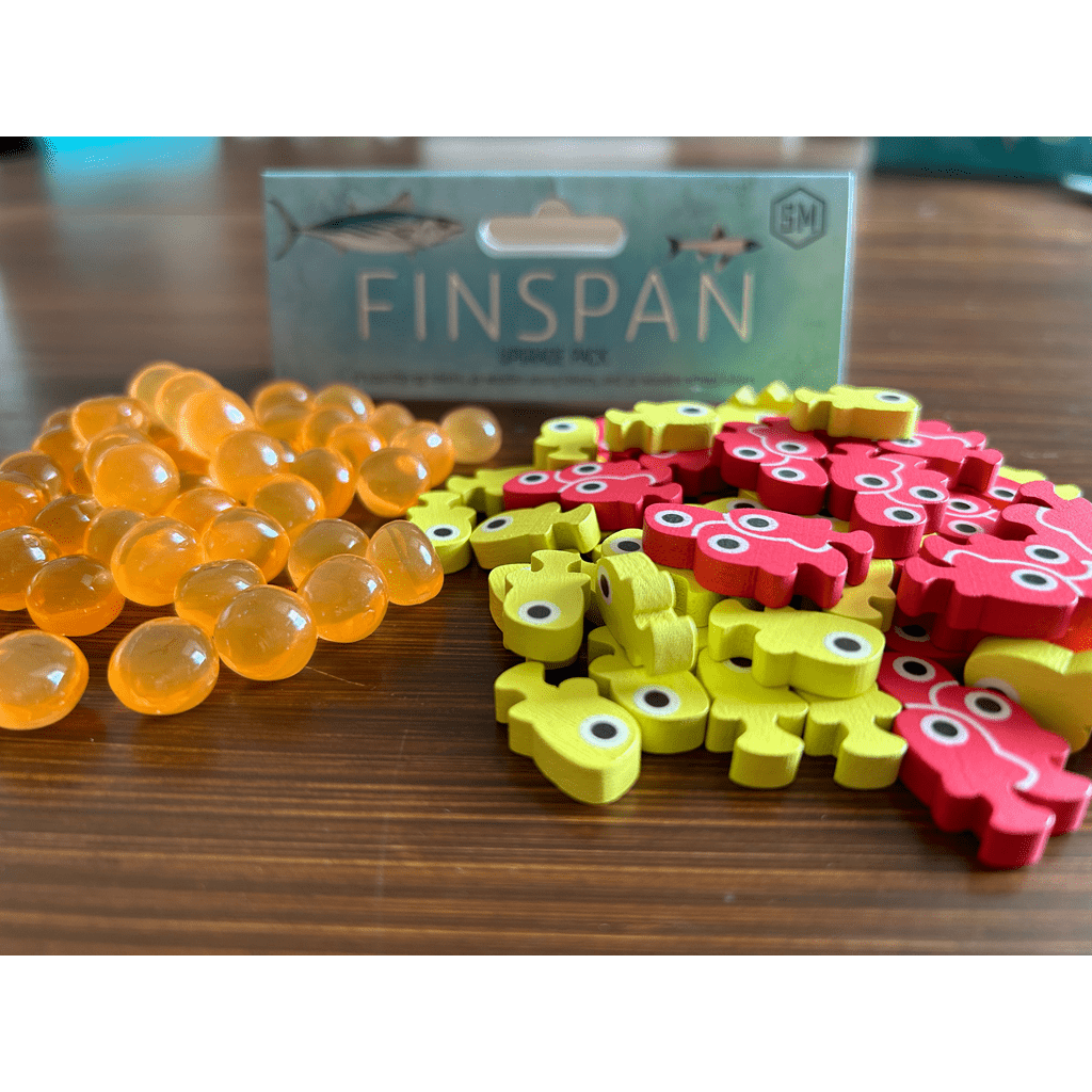 Orange translucent marbles, yellow and red fish-shaped wooden tokens, and the Finspan Upgrade Pack by Stonemaier Games are arranged on a wooden surface, ready to enhance your game experience.