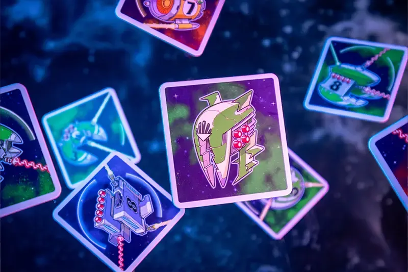 Colorful, illustrated cards with spaceships and numbers from Pegasus Spiele’s Light Speed: Arena float against a dark, starry background, hinting at a space-themed tile-laying game in play.