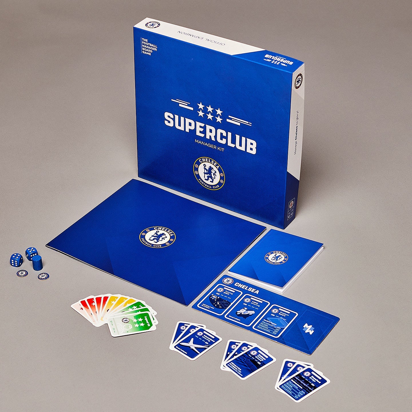 The Superclub: Chelsea Manager Kit by Superclub is displayed with the game box, manager folder, booklet, four blue dice, colored cards, blue club cards, and tokens neatly arranged on a gray surface.