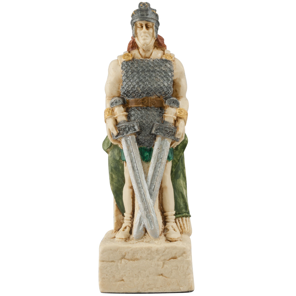 The Studio Anne Carlton Games Celtic & Viking Hand-painted Chess Pieces Set features a warrior in armor and helmet with crossed swords, dressed in green and brown, seated on a stone-like base—ideal for Viking or Celtic chess collections.