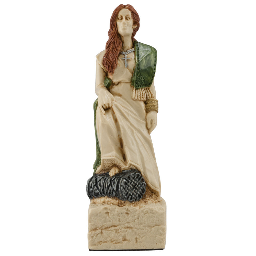A hand-painted figurine of a woman with long reddish-brown hair, in a cream dress and green shawl, sits on a carved stone with Celtic knots—part of the Studio Anne Carlton Games Celtic & Viking Chess Pieces Set.