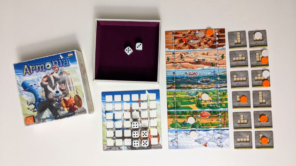 Armonia by Eagle-Gryphon Games is shown with its box, open lid, two dice, vibrant path boards, square grid cards with orange and white markers, plus a main board featuring dice and markers.