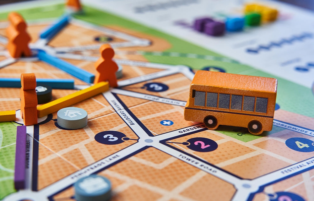 A close-up of Bus: Complete Edition by Capstone Games, showing a miniature orange bus, wooden pieces, player tokens, roads, numbered spaces, and city-themed map elements from this colorful public transport board game.