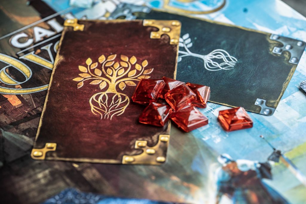 A close-up of Brotherwise Games’ Call to Adventure components, showing gold tree design cards, red gem tokens, and part of the vibrant fantasy storytelling game board.