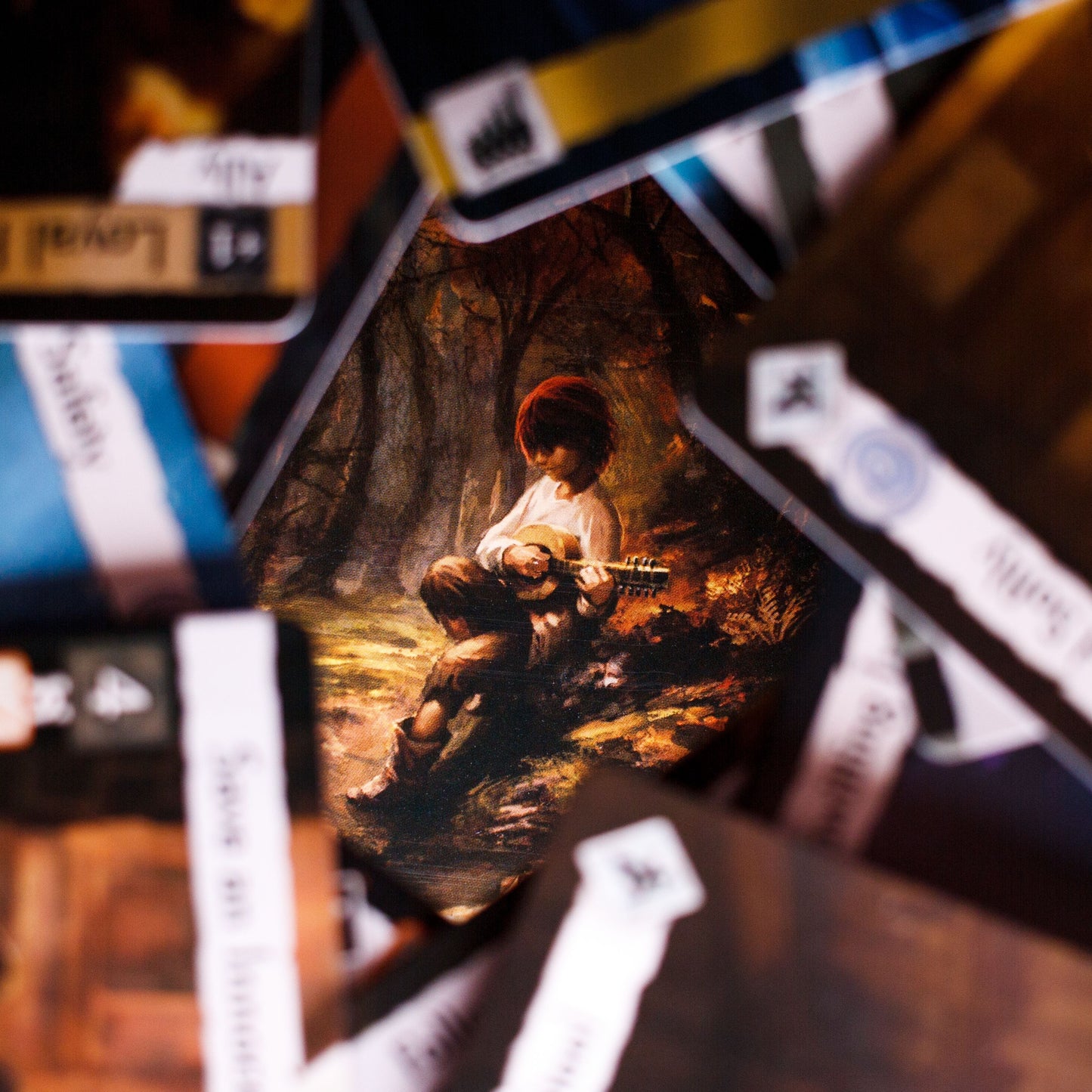 A card from Brotherwise Games’ Call to Adventure: Name of the Wind Expansion shows a person in a red hat playing a stringed instrument, surrounded by overlapping cards that evoke the enchanting world of the series.