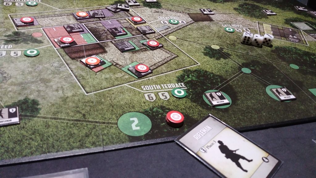 A close-up of Dan Verssen Games' Castle Itter wargame in play, showing a green map, circular tokens, dice, and player cards—including one with a "Fireman" silhouette—on a grassy board.