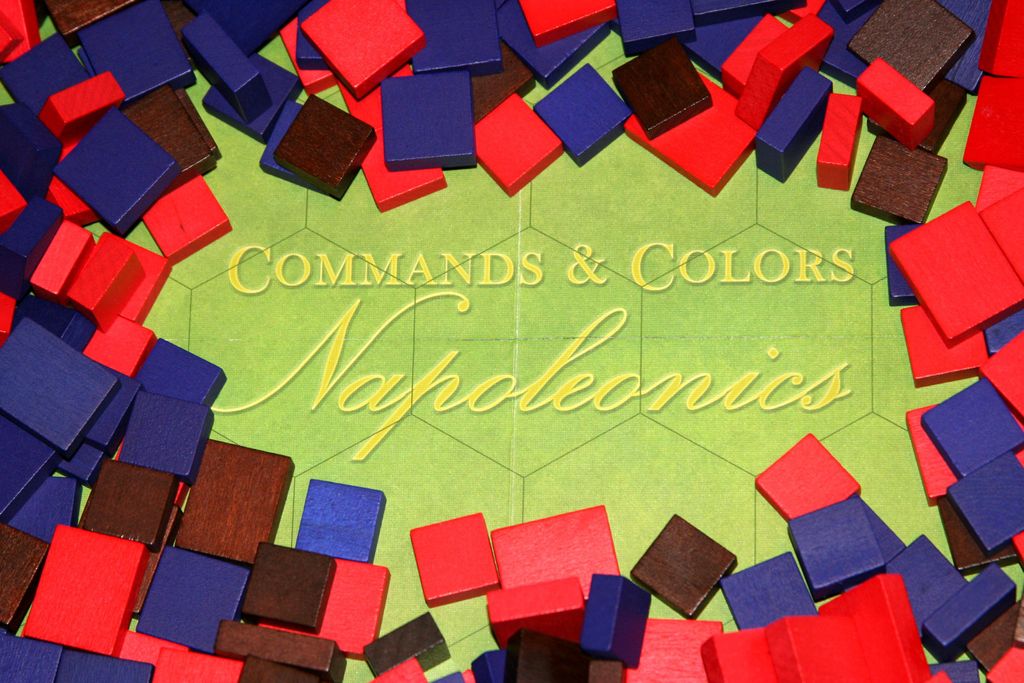 Commands & Colors: Napoleonics by GMT Games is at the center, with scattered red, blue, and brown wooden cubes surrounding the wargame board.