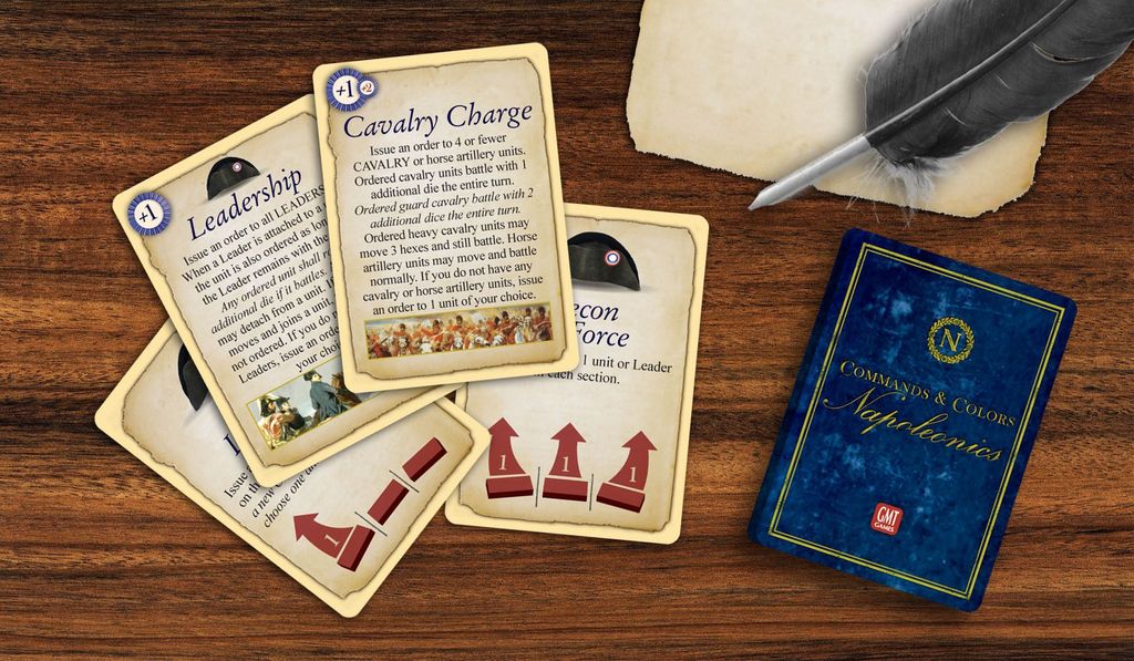 Three illustrated game cards labeled Leadership, Cavalry Charge, and Recon in Force are displayed on a wooden table with a feather quill, parchment, and a blue Commands & Colors: Napoleonics deck from GMT Games.