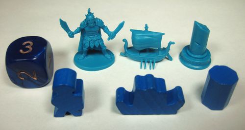A set of blue Cyclades board game pieces by Matagot features a numbered die, warrior figurine, ship, pillar, and unique Ancient Greek-inspired tokens arranged in a row on a white surface.