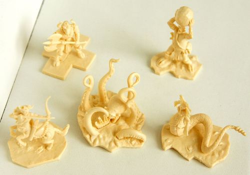 Five beige plastic figurines—warrior, tentacled monster, and more fantasy creatures—from the Cyclades board game by Matagot are displayed on a white surface, each on a uniquely shaped base.