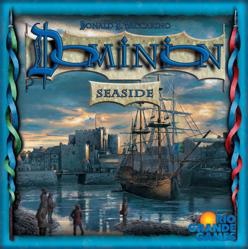 The box for Dominion: Seaside Expansion by Rio Grande Games features a seaside harbor at sunset with a large ship docked, people on the shore, waterfront buildings, and a distant castle—an eye-catching addition to the Dominion series.
