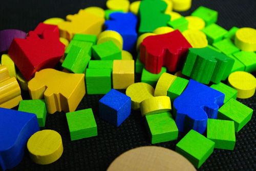 A vibrant pile of red, yellow, green, and blue wooden game pieces for Dungeon Lords by Czech Games Edition (CGE) includes cubes and circles—ideal for building dungeon layouts or hiring monsters on a black textured surface.