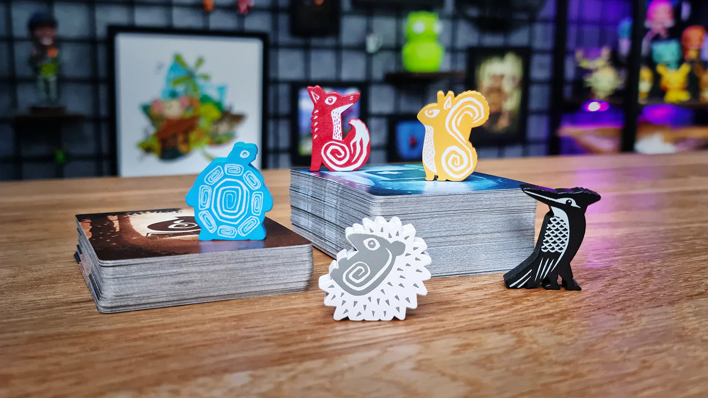 Five colorful animal tokens (turtle, fox, squirrel, hedgehog, woodpecker) surround a deck of cards on a wooden table—ready for an Emberleaf engine-building adventure by The City of Games amidst vibrant board game art.