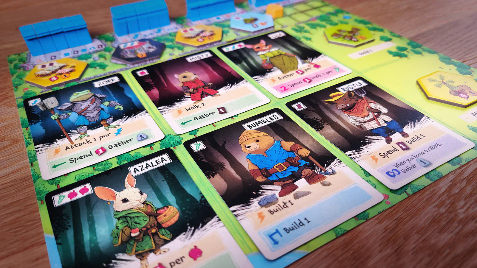 A close-up of The City of Games’ Emberleaf board game, showing illustrated animal character cards with abilities and actions, tokens, and a partially visible game board on a wooden table.