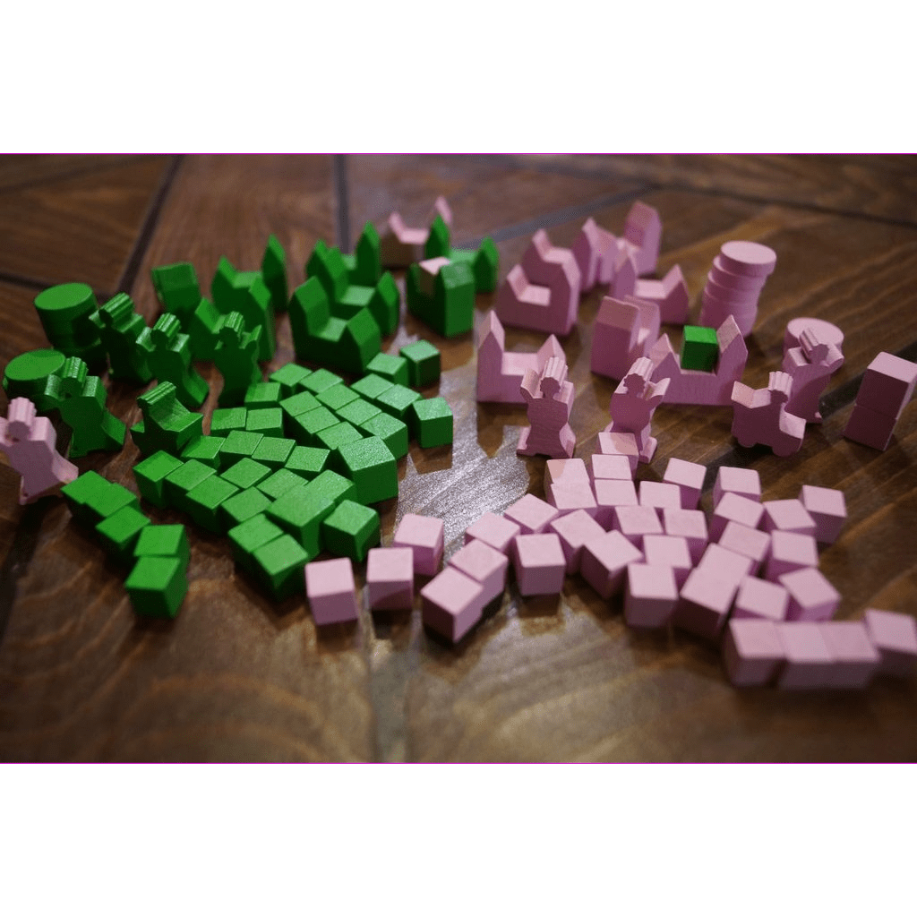 Small green and pink wooden game pieces from the Era of Tribes: 5/6 Player Expansion by Black Beacon Games, including cubes and various shapes, are spread out on a wooden surface.