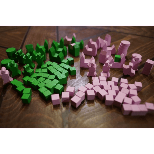 Small green and pink wooden game pieces from the Era of Tribes: 5/6 Player Expansion by Black Beacon Games, including cubes and various shapes, are spread out on a wooden surface.