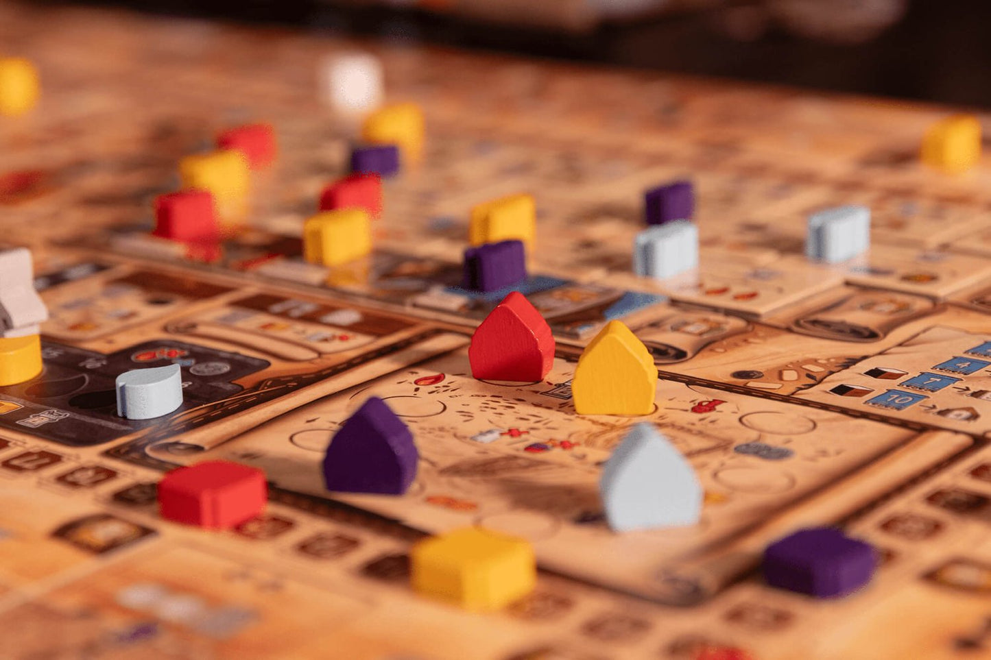 A close-up of Garphill Games' "Ezra and Nehemiah" shows colorful wooden pieces—red, yellow, purple, and blue—on a vibrant board with cards and symbols inspired by rebuilding the Jerusalem temple.