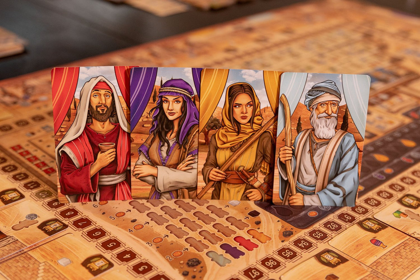 Four illustrated character cards from Garphill Games' "Ezra and Nehemiah" stand upright on a detailed board with tokens and score tracks, depicting men and women in Middle Eastern attire from the era of Cyrus the Great’s decree.