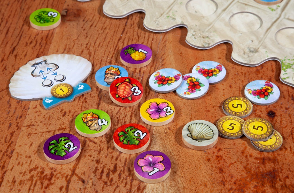 A tabletop scene from FYFE by Pegasus Spiele, an abstract tile-laying game featuring colorful flower, fruit, and number tokens, gold coins, a shell piece, scoring boards, and part of a sandy-hued board on wood.