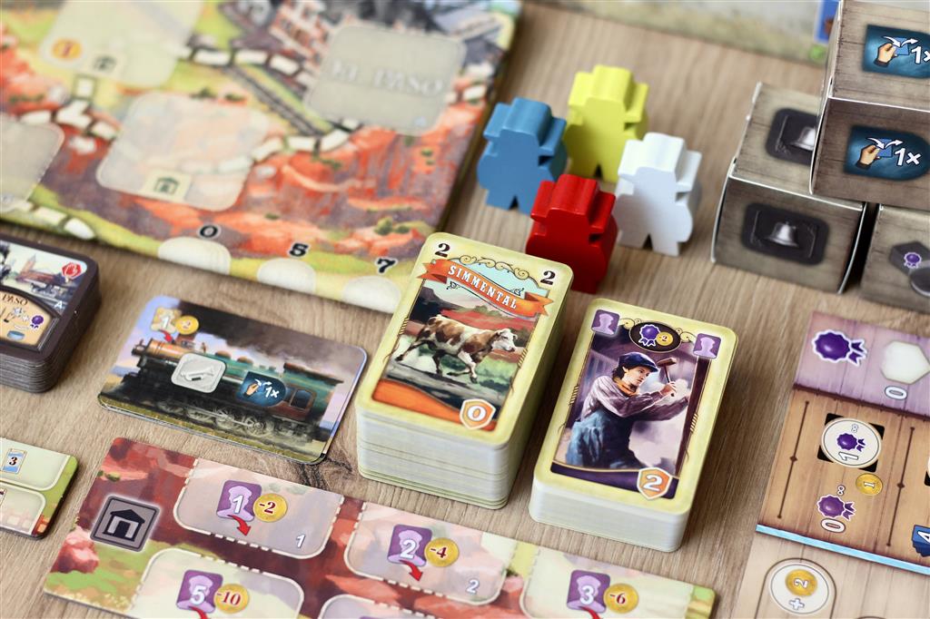 A close-up of Great Western Trail: El Paso by Lookout Games features cards with illustrations, colorful wooden meeples, and cattle trade pieces arranged on a wooden table.