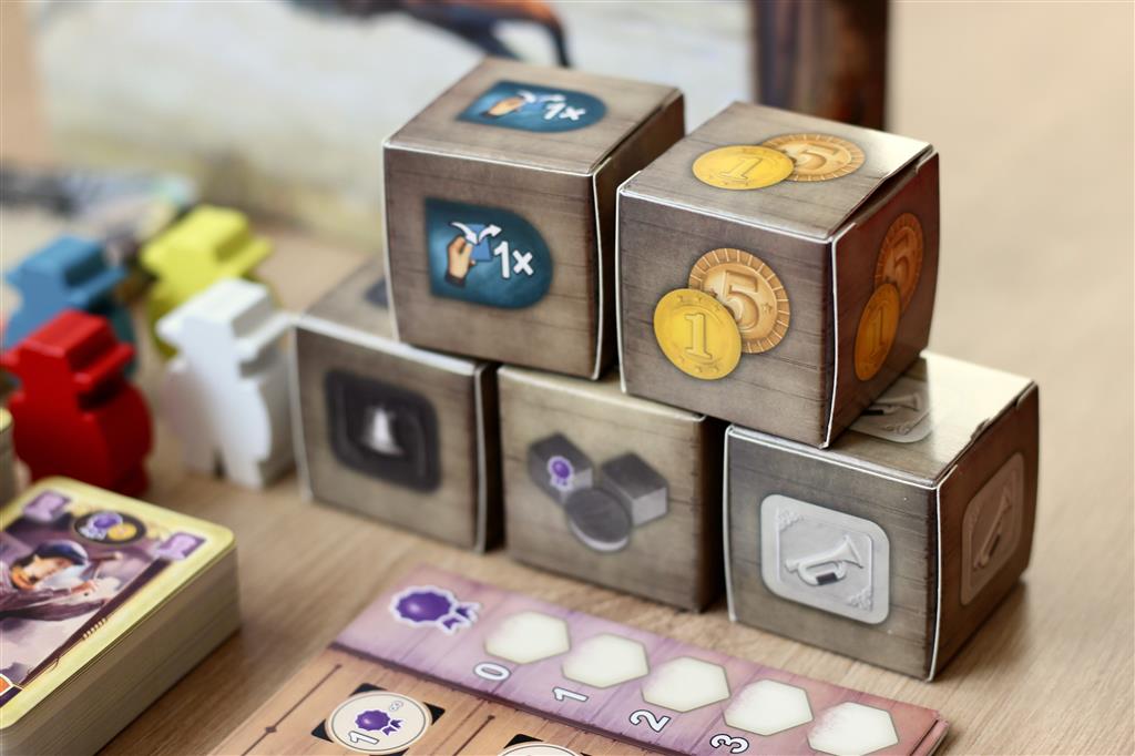 A close-up of Great Western Trail: El Paso by Lookout Games shows wooden animal tokens, illustrated cards, and stackable cardboard cubes with coin icons, capturing the cattle trade theme on a wooden surface.