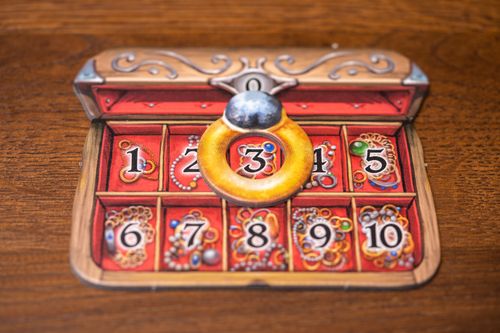 The Hallertau board game component by Lookout Games displays numbers 1–10 in ornate boxes, with a gold ring around the 3. Its background, resembling a treasure chest on wood, evokes agricultural and sheep breeding themes.