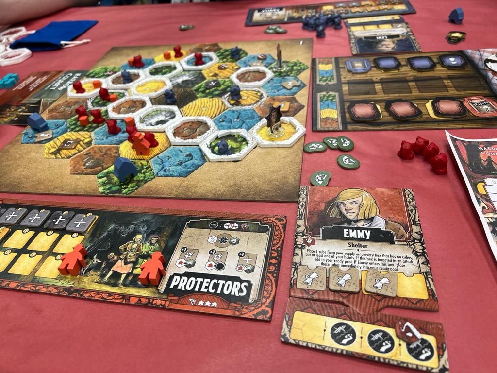 A game of Harrow County: The Game of Gothic Conflict by Off the Page Games is underway on a red table, featuring its hexagonal map, colored tokens, and asymmetric player boards like EMMY, highlighting tactical combat gameplay.