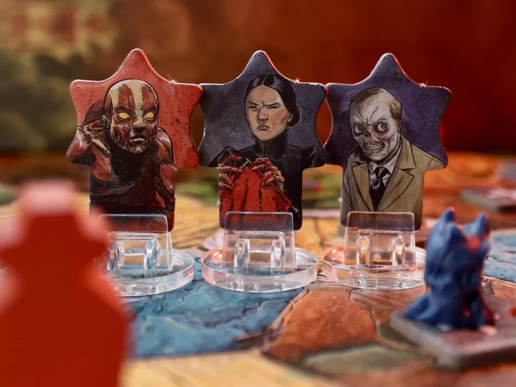 Three illustrated cardboard figures from Harrow County: The Game of Gothic Conflict by Off the Page Games—a red-skinned monster, a woman in black, and a sinister man—stand on a vibrant board, evoking this asymmetric game’s eerie cube tower action.