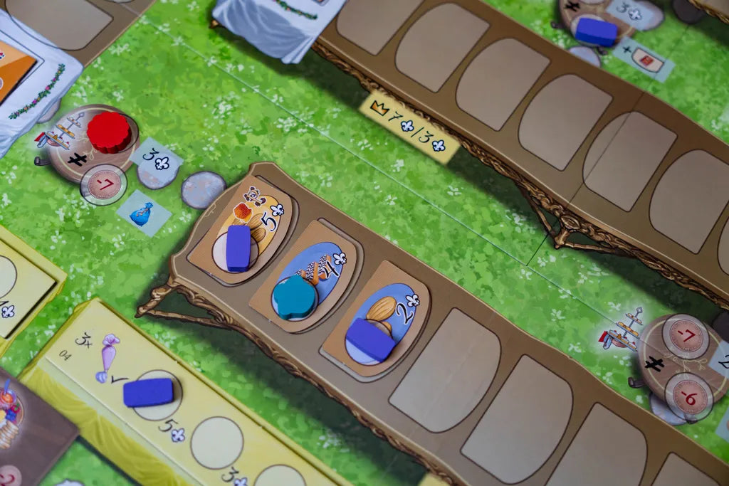 A close-up of Eagle-Gryphon Games' La Pâtisserie Rococo board game shows its vibrant Versailles Garden Festival setting, featuring green spaces, tokens, cards, and purple, orange, and blue pieces—possibly pastry chefs—on illustrated sections.