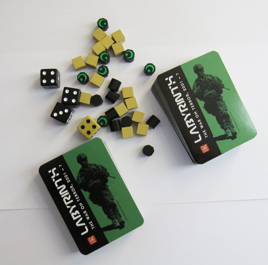 Labyrinth: The War on Terror, 2001 – ? by GMT Games is shown with two decks of cards, black and yellow dice, wooden cubes, and tokens on a white surface. The card cover displays a green-and-black soldier’s silhouette amid an al-Qaeda era theme.