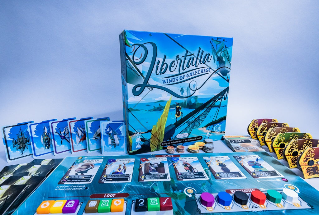 A setup of Stonemaier Games' Libertalia: Winds of Galecrest featuring the game box, cards, player boards, tokens, and treasure chests arranged on a blue surface with a nautical sky pirate theme.