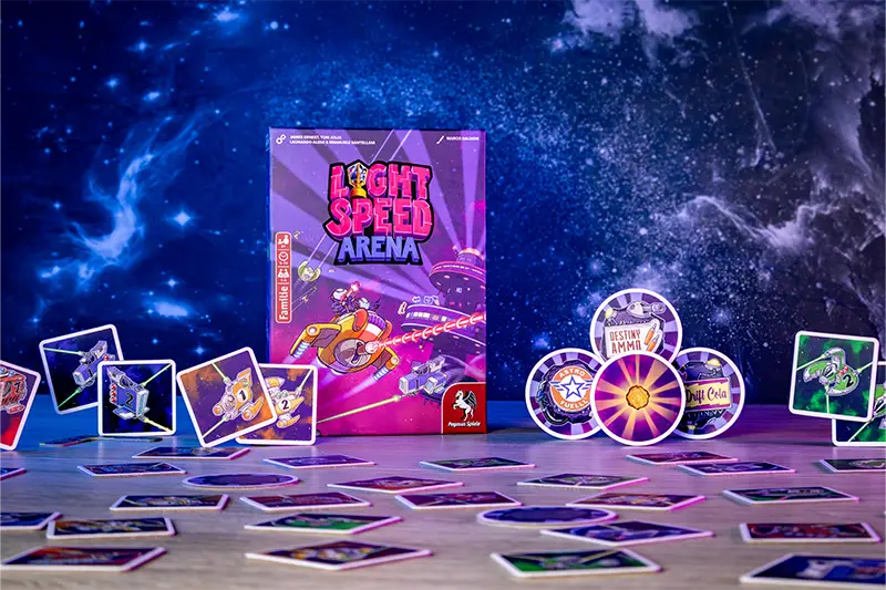 Light Speed: Arena by Pegasus Spiele is shown on a table with cards arranged before its vibrant box. A starry galaxy backdrop emphasizes the fast-paced, real-time sci-fi shooter card game adventure.