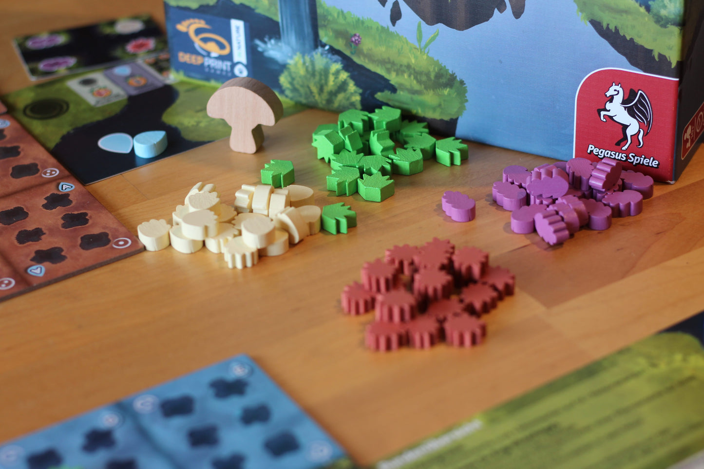 Colorful animal- and plant-shaped wooden pieces from Pegasus Spiele's Moorland board game are arranged on a table, inviting players to enjoy immersive habitat building and ecosystem management gameplay.