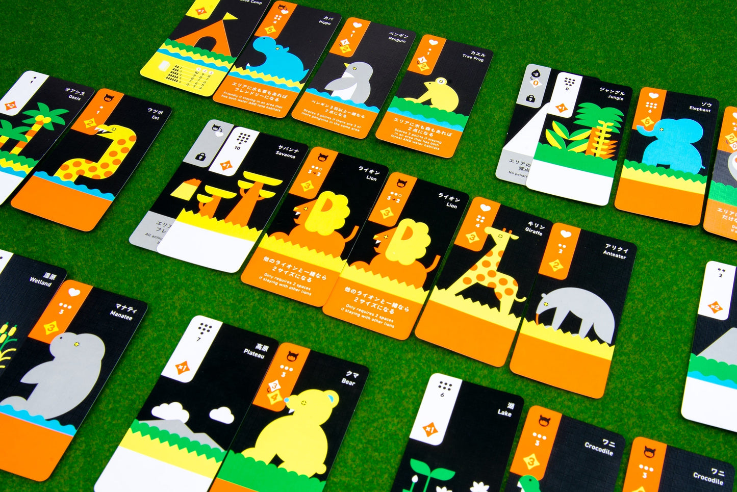 Moving Wild by Oink Games features colorful illustrated playing cards with animals, plants, and nature icons on a grass-like green surface. Inspired by national parks, each card has orange, yellow, and black blocks with Japanese text.