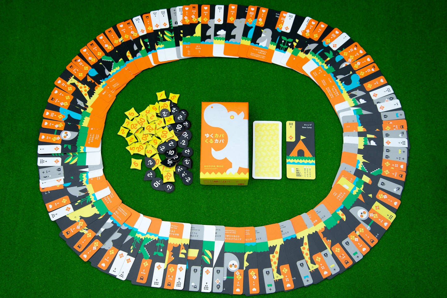 Moving Wild by Oink Games features an oval track of colorful cards—evoking animal migration—arranged on green felt around yellow tokens, black pieces, a card deck, and a center box with a white dinosaur illustration.