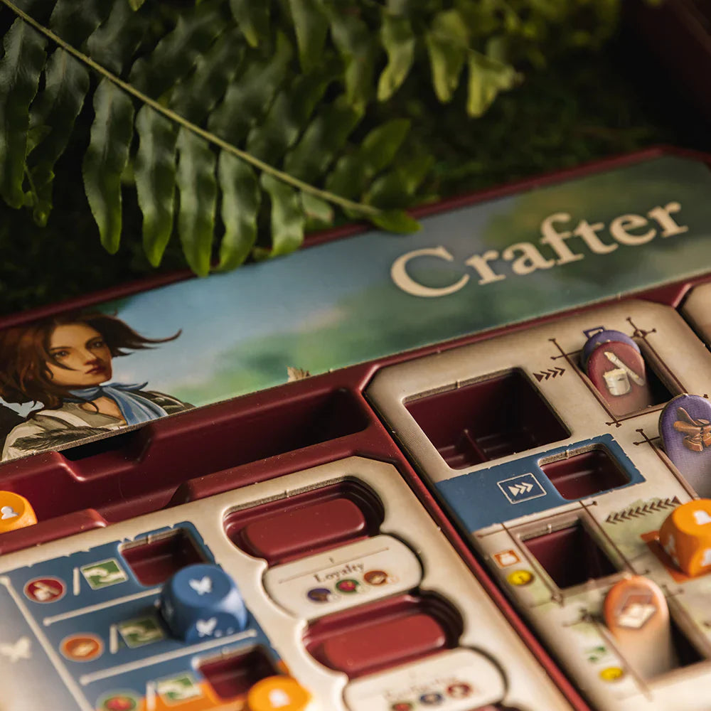 A close-up of Mythwind (Damaged) by Open Owl Studios, showing illustrated cards, tokens, and game pieces in a cooperative board game setup, with greenery and fern leaves in the background.