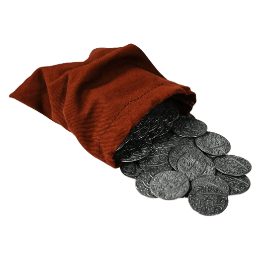 A small red cloth bag from Pax Pamir: Second Edition Metal Coins & Cloth Bag spills intricately designed metal coins onto a white surface.