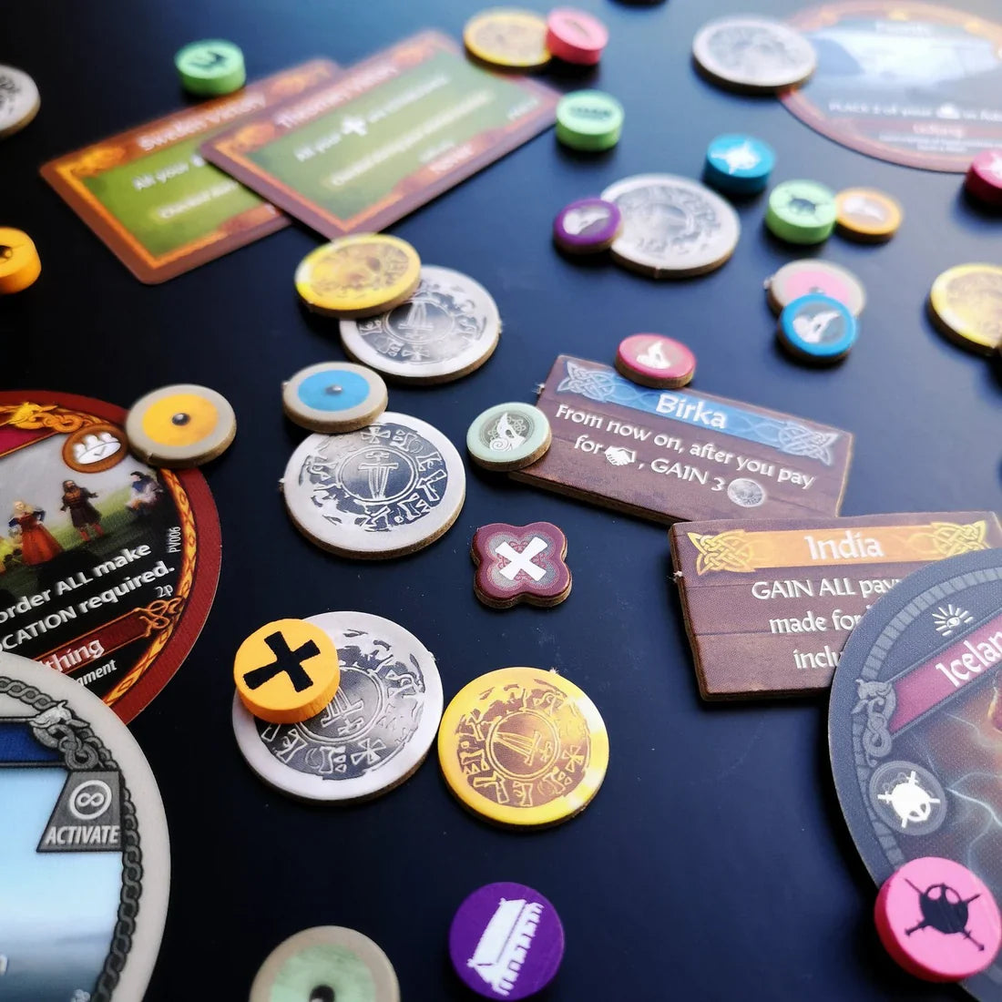 Colorful pieces, tokens, and cards from Pax Viking by Ion Game Design are spread across a dark surface, showcasing elements of this historical strategy game inspired by Viking exploration.