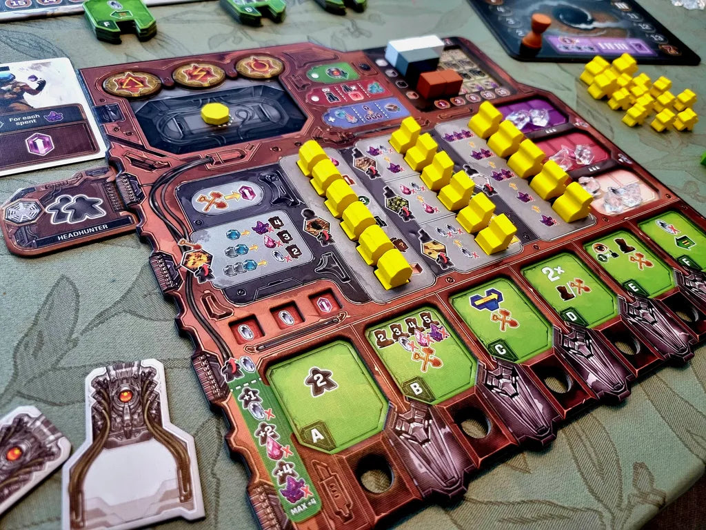 A close-up of Recall by Alion Games shows a vibrant engine-building board game setup with a detailed player board, yellow cubes, cards, and tokens on a patterned surface—evoking sci-fi strategy exploration.