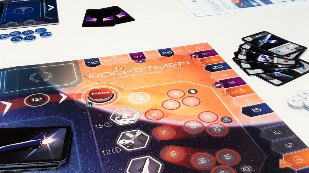 Rocketmen by Phalanx is set up on a white table, displaying cards, tokens, and a Mars-inspired space exploration board with planets, numbers, and hexagonal spaces.