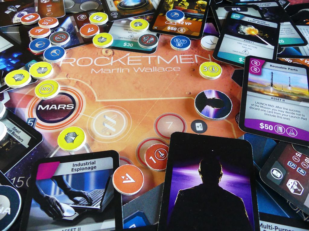 A close-up of Rocketmen by Phalanx highlights the deck-building gameplay with cards, vibrant tokens, and currency on a Mars-themed board, capturing the thrill of space exploration.