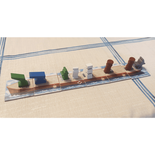 A Shipyard (2nd Edition): Wooden Components tile by Delicious Games features a wooden ship and colorful green, blue, white, brown, and gray pieces arranged on top, set on a beige tablecloth with blue lines.