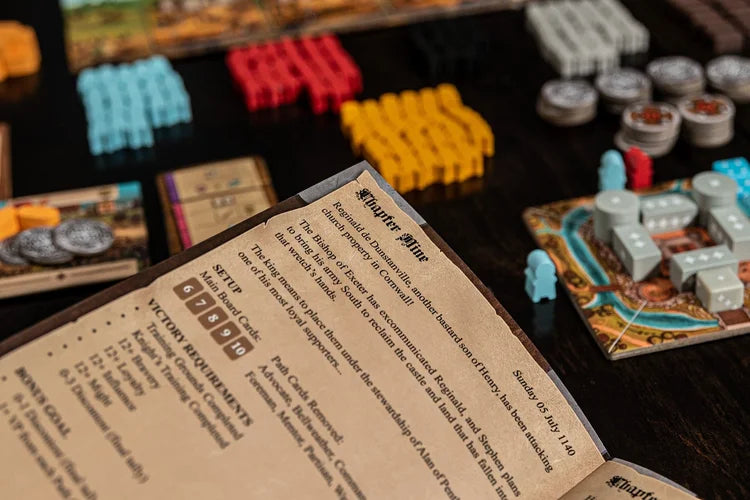 A close-up of The Anarchy rulebook by Renegade Game Studios, open on a dark table with colorful game tokens and pieces scattered around.