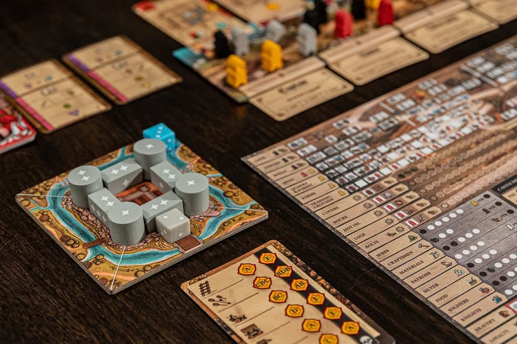 Colorful components—including cards, tokens, castle-shaped pieces, and tracking boards—are arranged on a dark wooden table, ready for play in The Anarchy by Renegade Game Studios, an engaging medieval strategy board game.