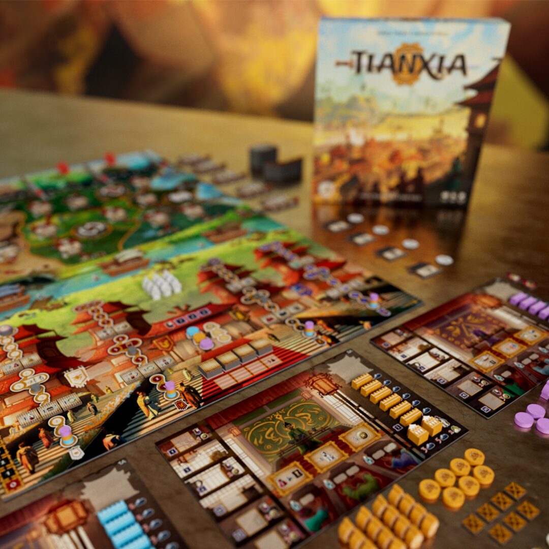 The table is set with vibrant tokens, cards, and player boards from Tianxia by Board & Dice. The game box, adorned with East Asian-inspired art from the Warring States era, stands prominently in the background.