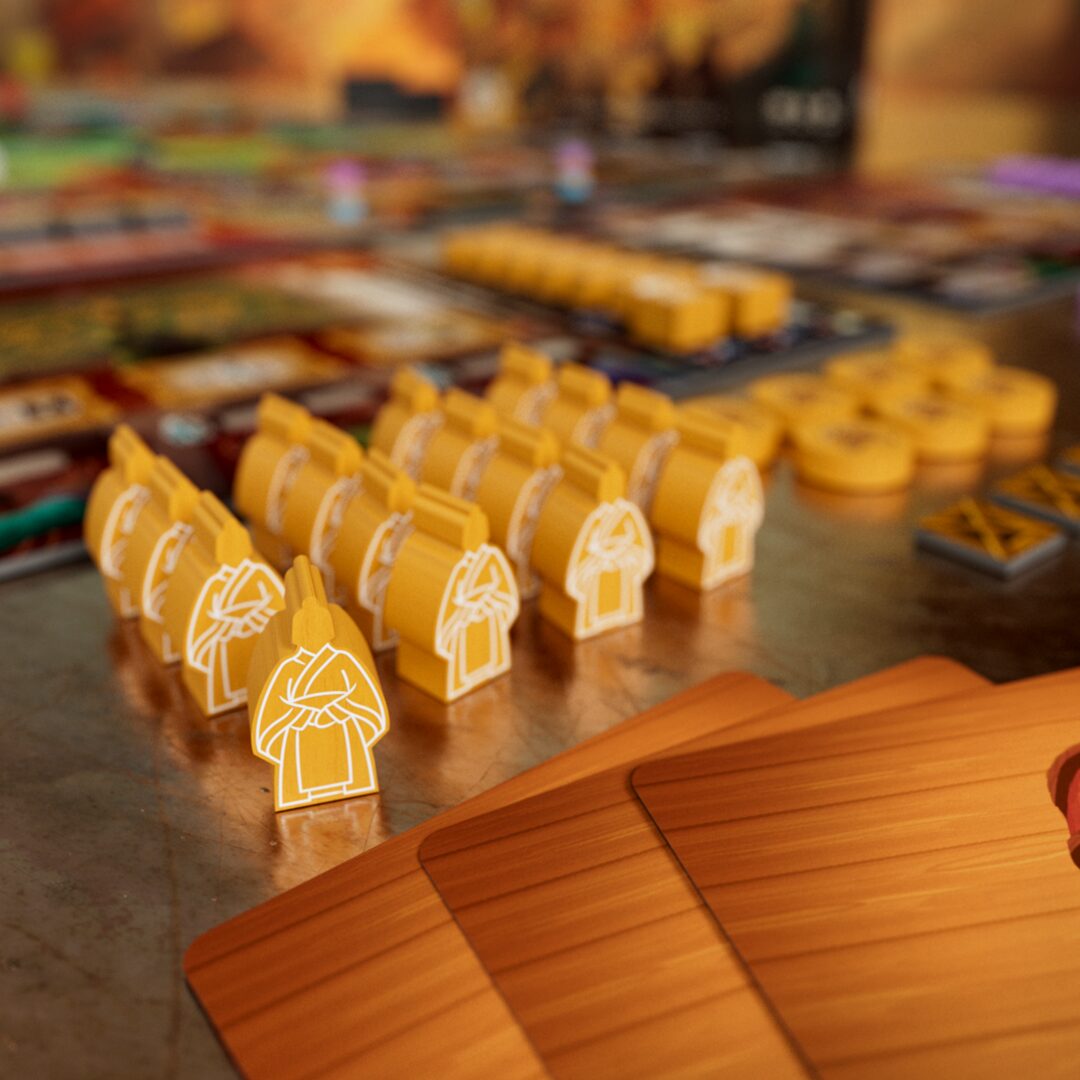 Close-up of Tianxia by Board & Dice, a strategy board game set in the Warring States period, featuring yellow wooden robed tokens, stacks of circular yellow tokens, and three brown cards on a textured surface.
