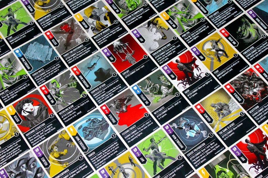 A diagonal grid displays colorful trading cards from Unmatched: Cobble & Fog by Restoration Games. Each features unique artwork, icons, and text on vivid green, yellow, red, and blue backgrounds in this asymmetrical fighting game.