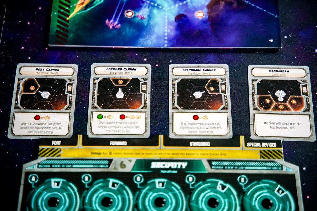 A close-up of Plaid Hat Games’ Wandering Galaxy: A Crossroads Game shows four cards—Port Cannon, Forward Cannon, Starboard Cannon, and Macguffanium—arranged above a control panel labeled Security.